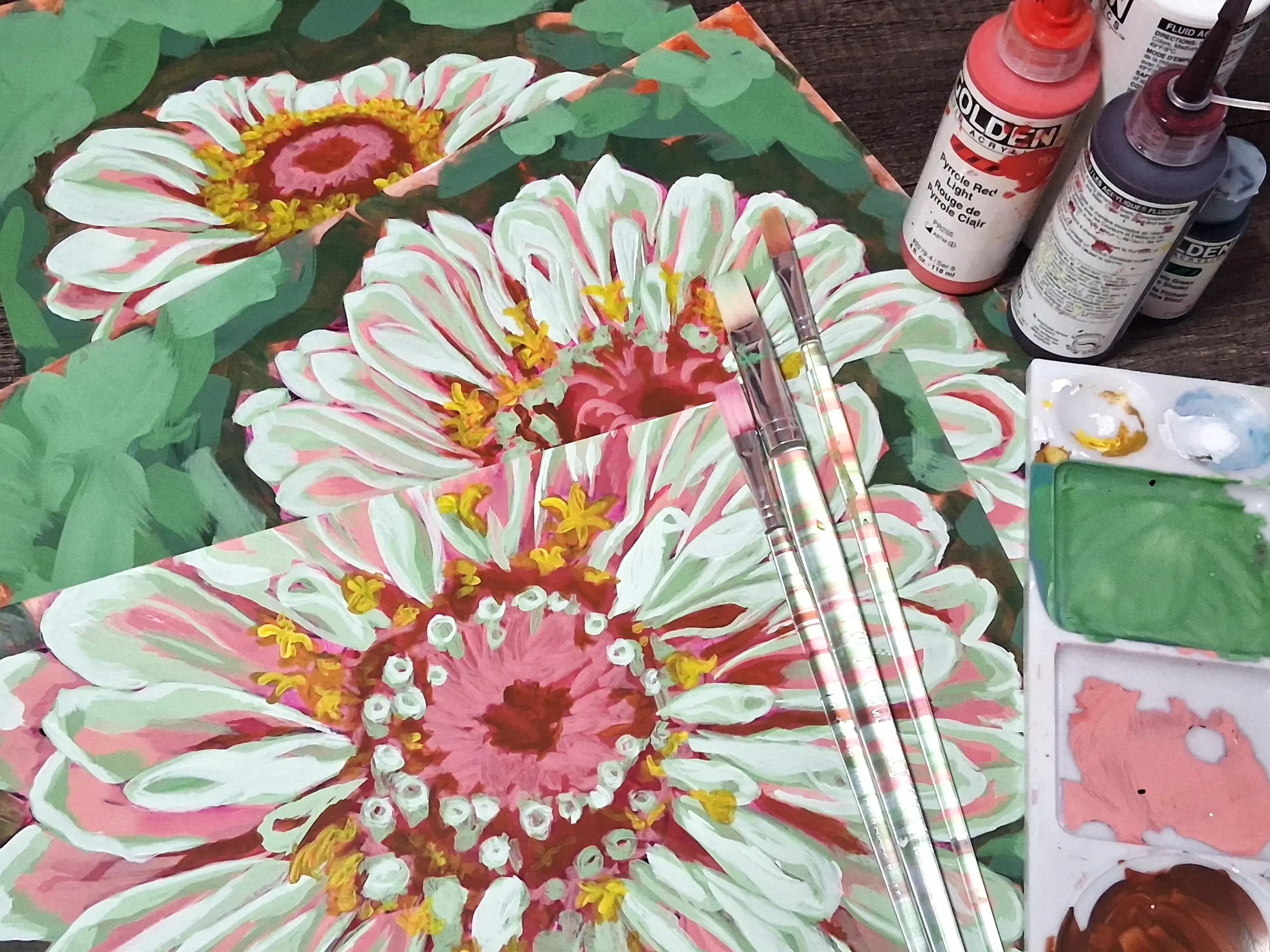 Hand-painted floral illustrations on a desk surrounded by acrylic paint bottles and paintbrushes.