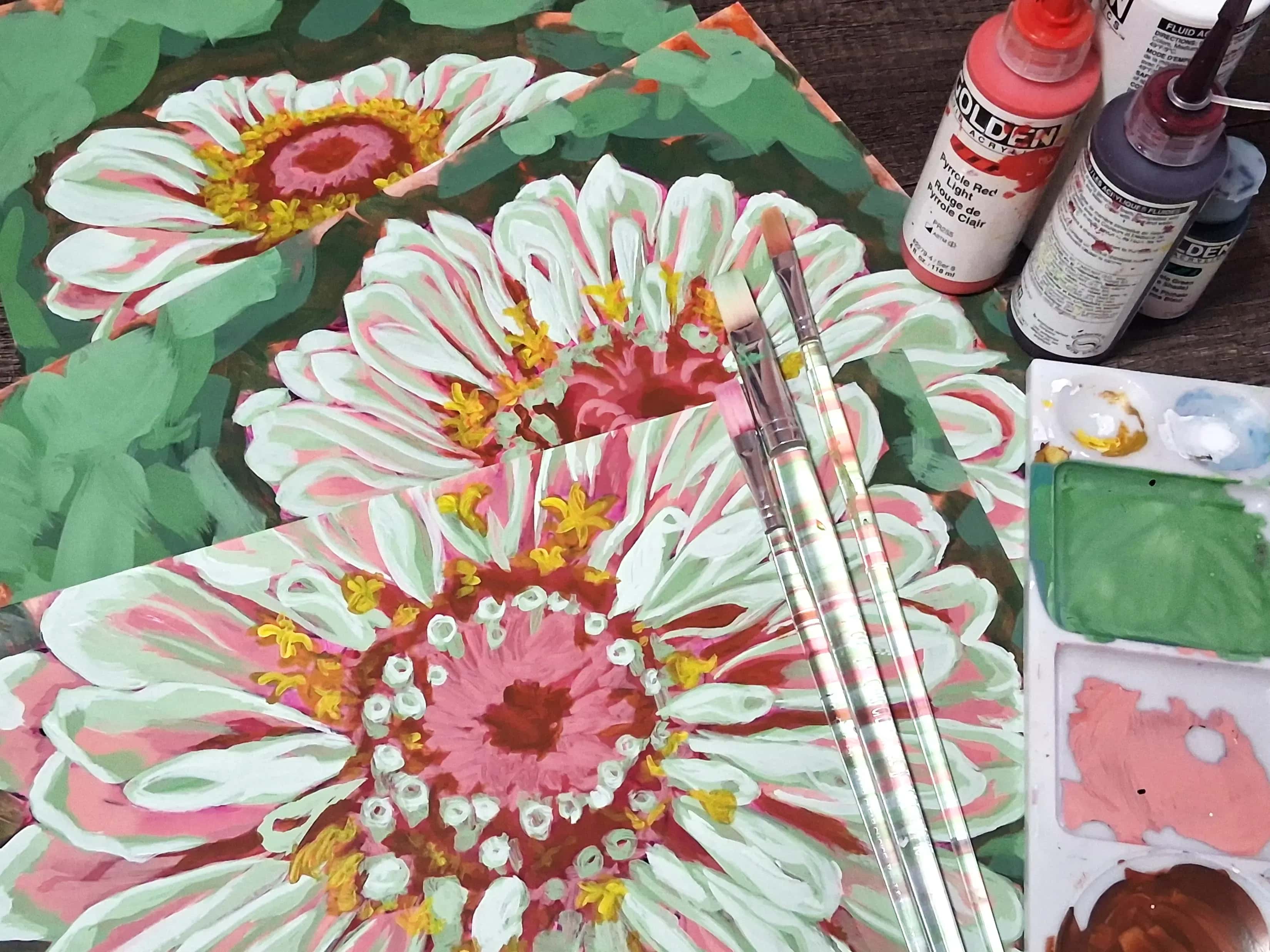Hand-painted floral illustrations on a desk surrounded by acrylic paint bottles and paintbrushes.